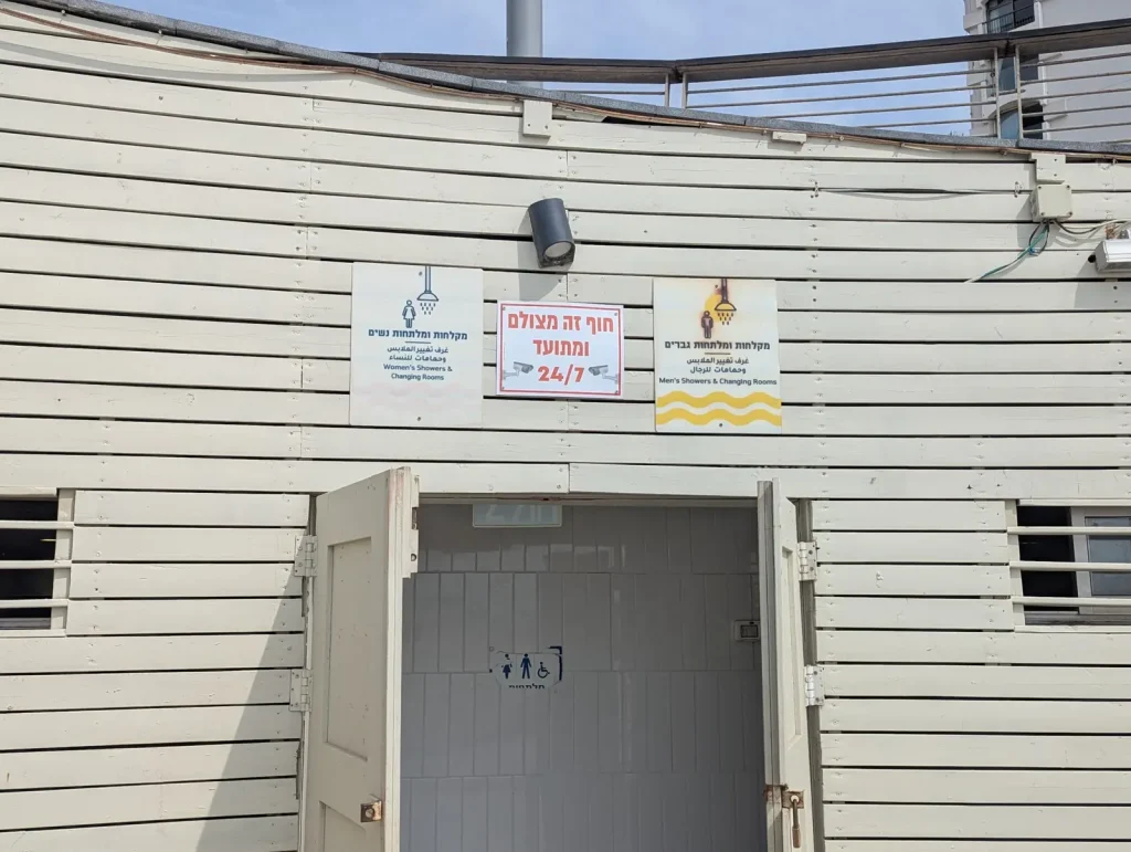 Beach toilets and showers building with a sign saying the beach is filmed 24/7