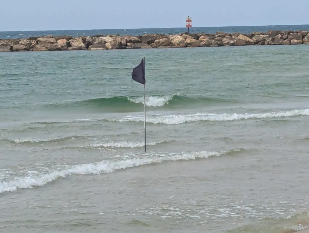 A black flag standing in the sea in front of the breakwater