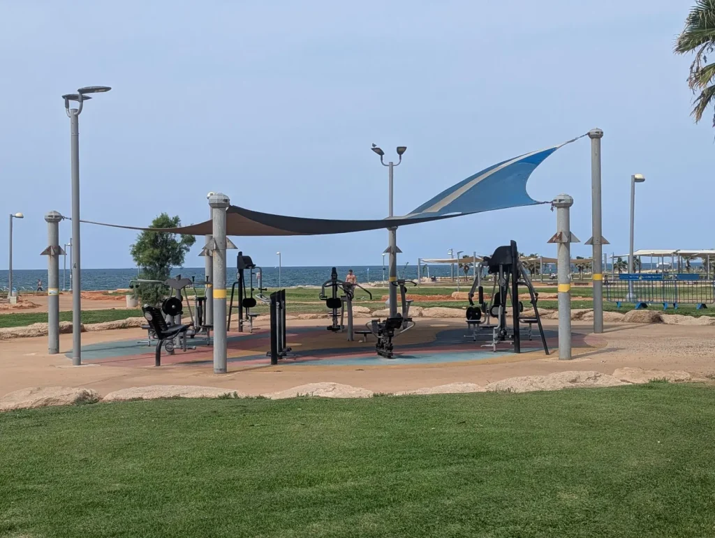 Shaded outdoor gym equipment in Charles Clore Park by the sea