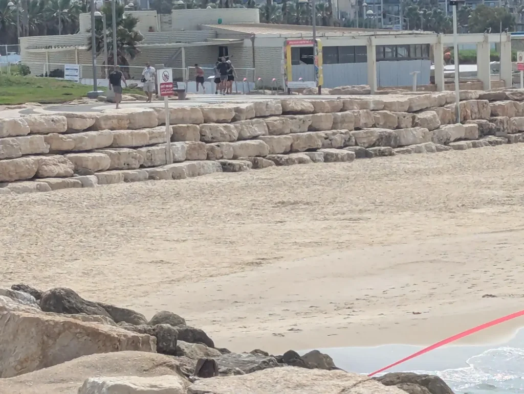 Rock wall and no-swimming sign at the edge of Charles Clore Beach
