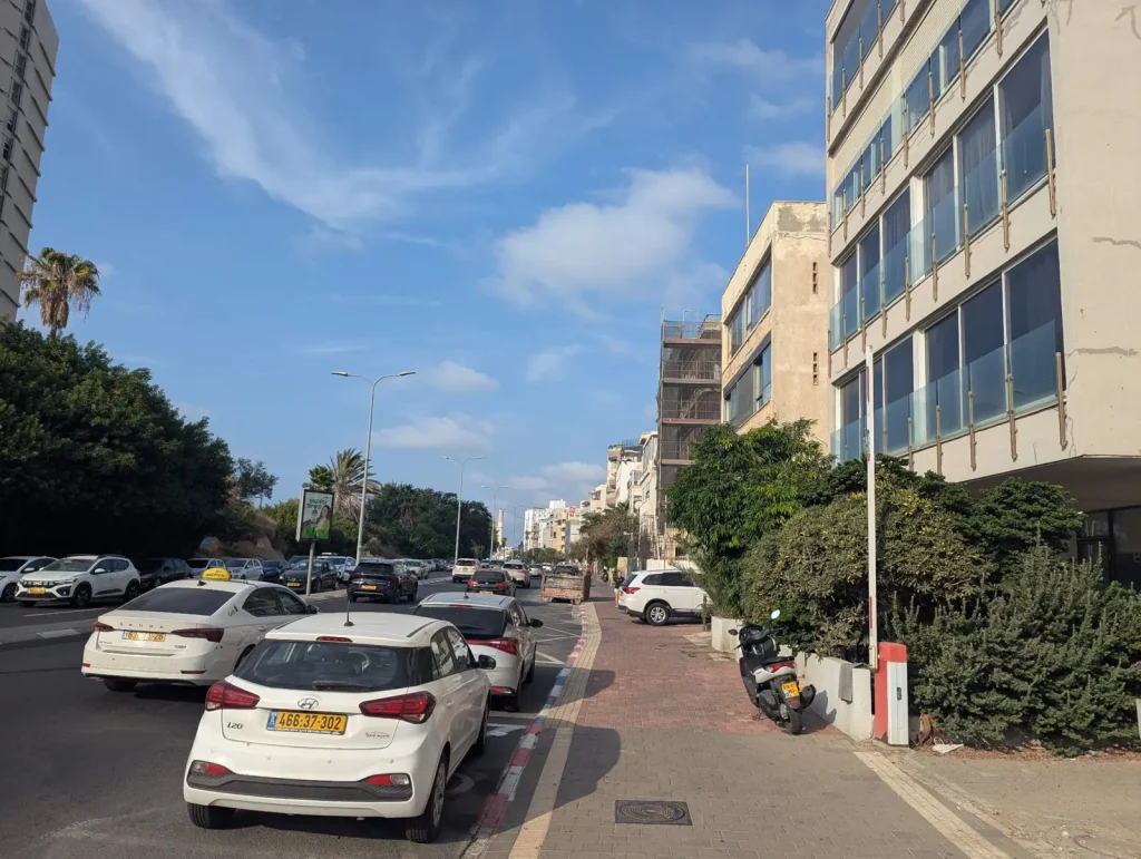 Looking up Hayarkon Street with parked cars and apartment buildings