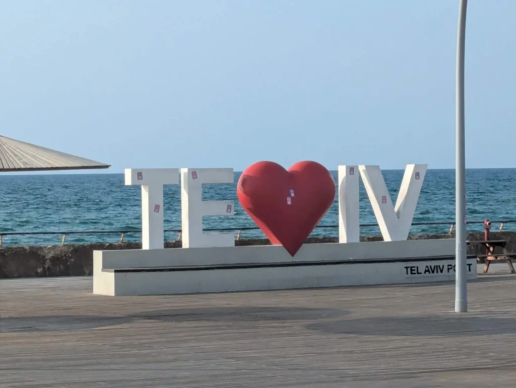 TLV sign with a red heart on the Tel Aviv Port boardwalk facing the sea