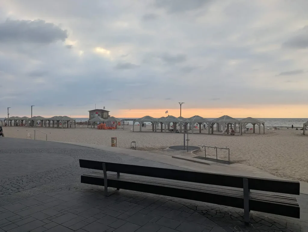 Bench facing Jerusalem Beach with shade huts on the sand