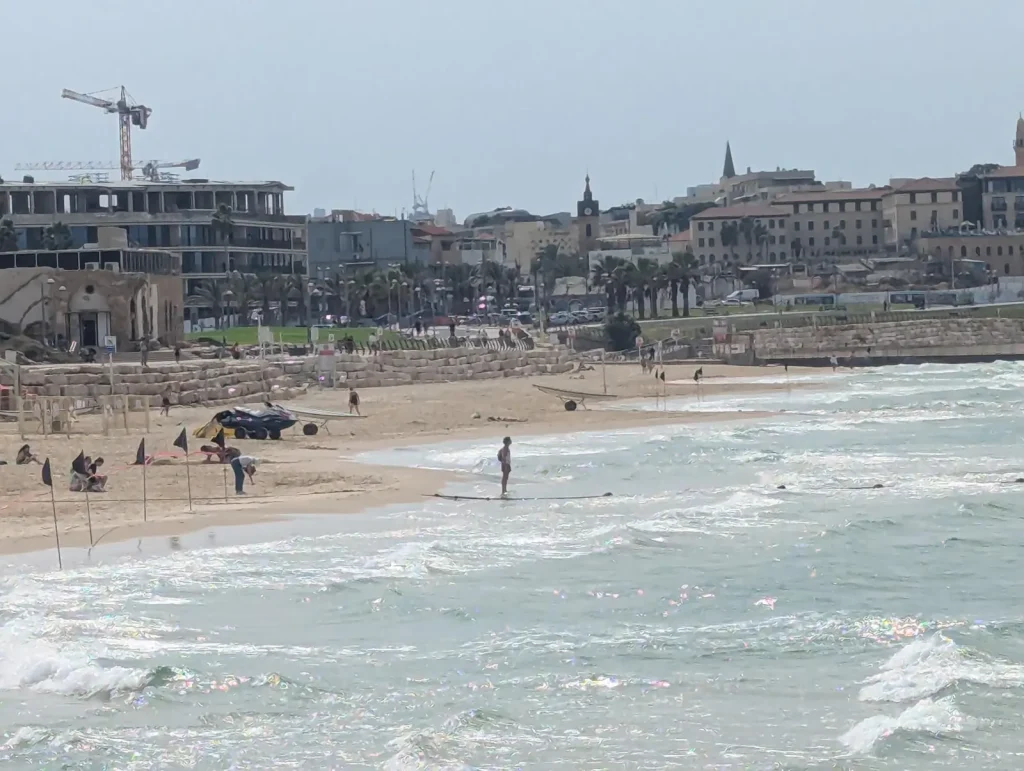 Swimmer near black flags at Maravi Beach with Jaffa behind