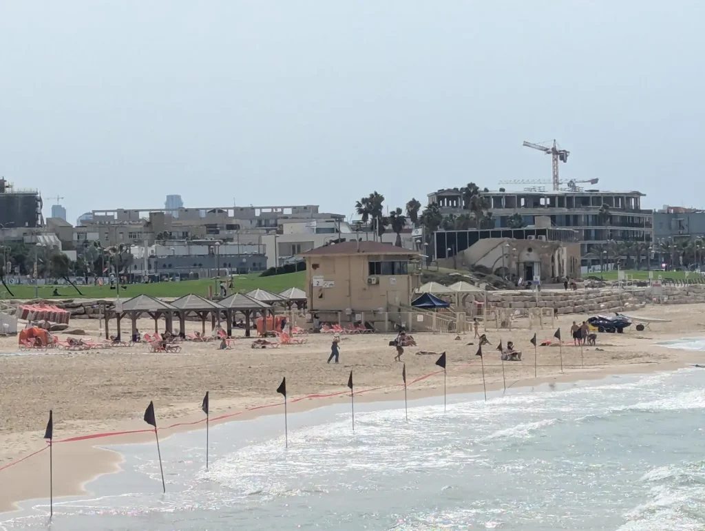 Black flags along the waterline at Maravi Beach with the lifeguard tower behind