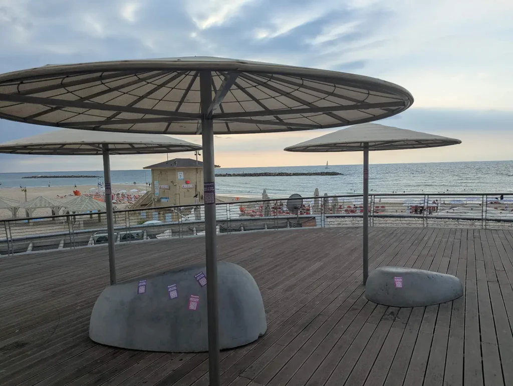 Rounded benches under umbrella shades on a wooden promenade deck by the sea