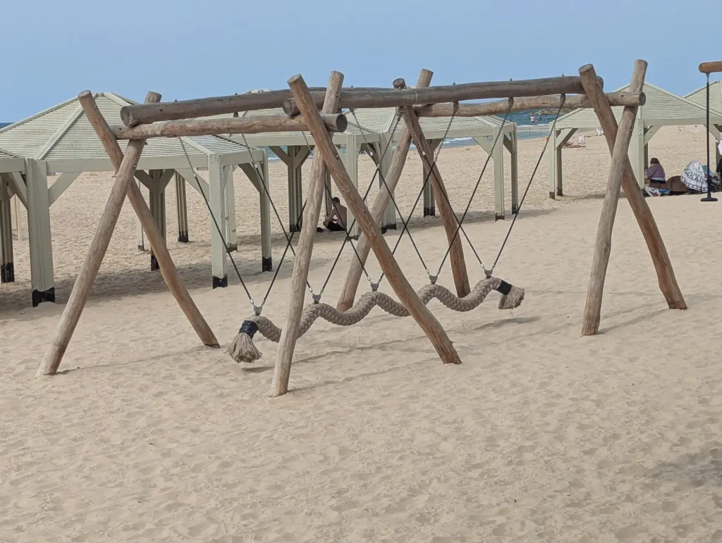 Rope swings at a beach playground under shade huts